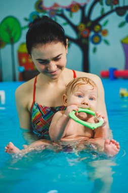 Havuzda yüzen bir bebek. Yeni doğmuş bir çocuğa koçla havuzda yüzmeyi öğretmek.