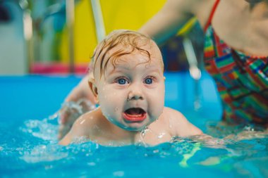Bir bayan antrenör bebeğe havuzda yüzmeyi öğretir ve ellerini destekler. Havuzda yüzen bir bebek. Yeni doğmuş bir çocuğa havuzda yüzmeyi öğretiyorum.