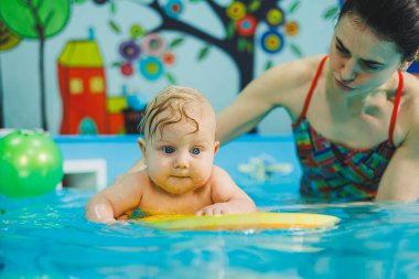 Yeni doğan çocukları yüzmeye alıştırmak için yüzme havuzu. Havuzda yüzen bir bebek. Yeni doğmuş bir çocuğa koçla havuzda yüzmeyi öğretmek.