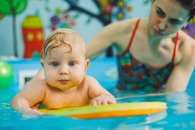 Bir bayan antrenör bebeğe havuzda yüzmeyi öğretir ve ellerini destekler. Havuzda yüzen bir bebek. Yeni doğmuş bir çocuğa havuzda yüzmeyi öğretiyorum.
