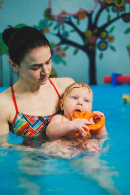 Bir bayan antrenör bebeğe havuzda yüzmeyi öğretir ve ellerini destekler. Havuzda yüzen bir bebek. Yeni doğmuş bir çocuğa havuzda yüzmeyi öğretiyorum.