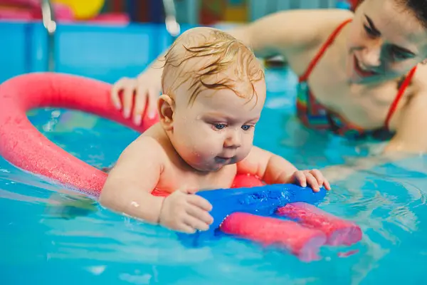 A female trainer teaches a baby to swim in the pool and supports his hands. Baby swimming in the pool. Teaching a newborn boy to swim in the pool