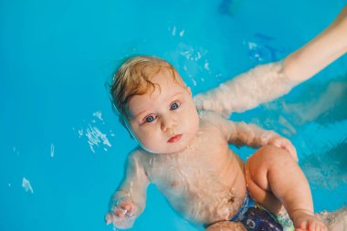 Yeni doğmuş bir çocuğa koçla havuzda yüzmeyi öğretiyorum. Bebek yüzme kursları. Çocuk havuzda yüzüyor.