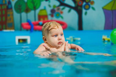 Yeni doğan çocukları yüzmeye alıştırmak için yüzme havuzu. Havuzda yüzen bir bebek. Yeni doğmuş bir çocuğa koçla havuzda yüzmeyi öğretmek.