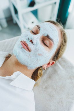 Yüzünde kremayla gülümseyen genç ve güzel bir kadın. Yüz derisi için bakım maskesi