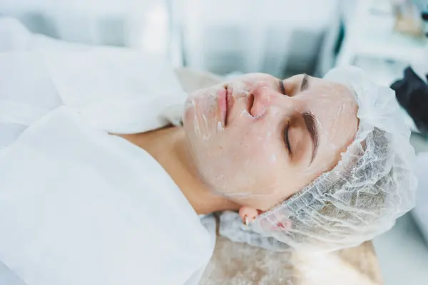 The office of a dermatologist or cosmetologist, a woman lies with a mask on her face. Facial skin care. Close-up of a woman's face with a white cosmetic mask
