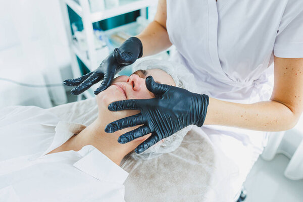 Офис косметолога, надевающего маску на лицо женщины в спа-салоне, вид сверху. Эстетическая процедура. Уход за кожей лица.