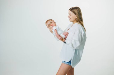 Genç bir anne, beyaz bir arka planda yeni doğmuş bir bebeği elinde tutuyor. Annelik kavramı. Yeni doğmuş bir bebeğin ilk ayı