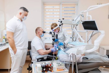 Dişçi dişçi ofisinde. Beyaz üniformalı bir dişçi bir hastanın dişlerini diş mikroskobuyla tedavi eder. Diş hekimliği