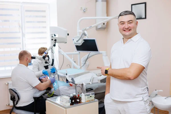The dentist is in his dental office. A dentist in a white uniform treats a patient's teeth with a dental microscope. Dental office