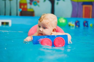 Yüzme havuzunda yeni doğmuş bir çocuğun eğitimi. Bebekler için bir havuz. Çocuk gelişimi. Küçük bir çocuk havuzda yüzmeyi öğreniyor.