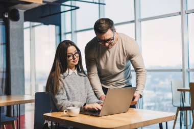 Erkek ve bayan meslektaşlar modern bir ofiste bir proje üzerinde birlikte çalışıyorlar. Ofisteki işçiler uydunun arkasında dizüstü bilgisayarla çalışıyorlar. Astın ve yöneticin.