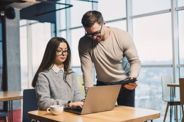 Erkek ve bayan meslektaşlar modern bir ofiste bir proje üzerinde birlikte çalışıyorlar. Ofisteki işçiler uydunun arkasında dizüstü bilgisayarla çalışıyorlar. Astın ve yöneticin.