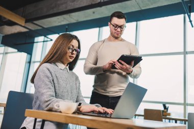 Erkek ve bayan meslektaşlar modern bir ofiste bir proje üzerinde birlikte çalışıyorlar. Ofisteki işçiler uydunun arkasında dizüstü bilgisayarla çalışıyorlar. Astın ve yöneticin.