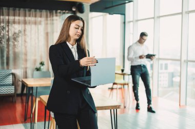 Ofisinde dizüstü bilgisayarı olan modern bir iş kadınının portresi. Ofiste çalışan, siyah takım elbiseli bir iş kadını.
