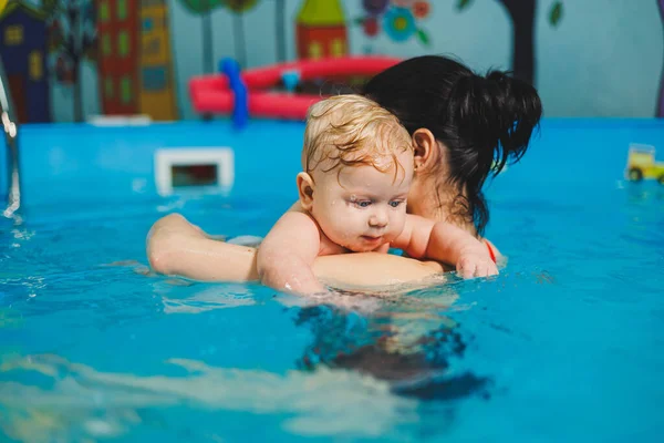 Training of a newborn baby in the pool with a swimming coach. A pool for babies. Child development. A small child learns to swim in the pool