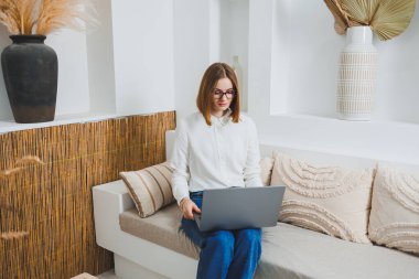 Genç serbest çalışan kadın kanepede oturuyor ve dizüstü bilgisayarda çalışıyor, dizüstü bilgisayarda film izliyor, çalışıyor, blog yazıyor, rahatlıyor ve internette sohbet ediyor..