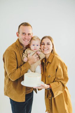 Mutlu genç anne ve baba yeni doğan oğullarını kollarına alıp ona pasta veriyorlar. Ebeveynler doğum günlerini küçük oğullarıyla kutluyorlar. Aile tatili kavramı.