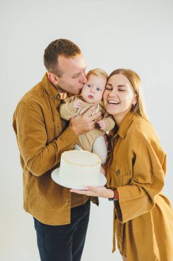 Mutlu genç anne ve baba yeni doğan oğullarını kollarına alıp ona pasta veriyorlar. Ebeveynler doğum günlerini küçük oğullarıyla kutluyorlar. Aile tatili kavramı.