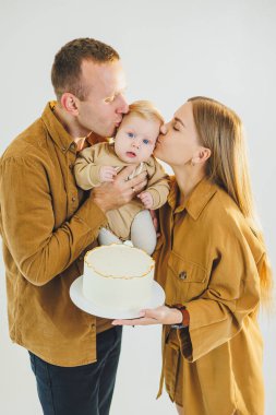Mutlu genç anne ve baba yeni doğan oğullarını kollarına alıp ona pasta veriyorlar. Ebeveynler doğum günlerini küçük oğullarıyla kutluyorlar. Aile tatili kavramı.
