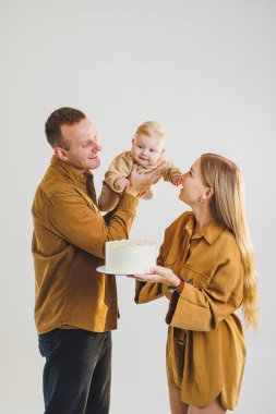 Mutlu genç anne ve baba yeni doğan oğullarını kollarına alıp ona pasta veriyorlar. Ebeveynler doğum günlerini küçük oğullarıyla kutluyorlar. Aile tatili kavramı.