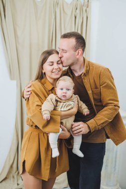 Mutlu bir anne ve baba 4 aylık oğullarını kollarında tutuyor. Mutlu ebeveynlerin yeni doğmuş bir bebekle çekilmiş aile fotoğrafı. Aile kavramı