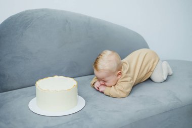 4 aylık küçük bir çocuk tatlı bir pastaya doğru sürünüyor. Yeni doğmuş bej elbiseli bir çocuk kanepenin üzerinde kekin üzerinde sürünüyor..