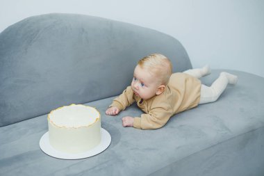4 aylık küçük bir çocuk tatlı bir pastaya doğru sürünüyor. Yeni doğmuş bej elbiseli bir çocuk kanepenin üzerinde kekin üzerinde sürünüyor..