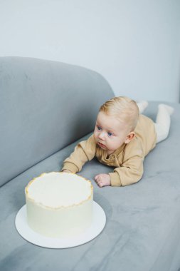 4 aylık küçük bir çocuk tatlı bir pastaya doğru sürünüyor. Yeni doğmuş bej elbiseli bir çocuk kanepenin üzerinde kekin üzerinde sürünüyor..
