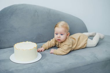 4 aylık küçük bir çocuk tatlı bir pastaya doğru sürünüyor. Yeni doğmuş bej elbiseli bir çocuk kanepenin üzerinde kekin üzerinde sürünüyor..