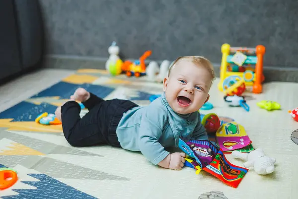 Dört aylık bir çocuk bir paspasın üzerinde yatıyor ve sürünüyor. Bebek termal bir mindere uzanıp oynuyor. Yeni doğmuş bir çocuğun öz gelişimi. Çocuk gelişimi için oyuncaklar.