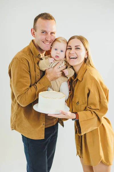 Mutlu genç anne ve baba yeni doğan oğullarını kollarına alıp ona pasta veriyorlar. Ebeveynler doğum günlerini küçük oğullarıyla kutluyorlar. Aile tatili kavramı.