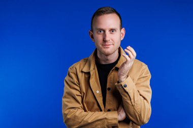 Kahverengi gömlekli mavi arka planda kendine güvenen neşeli bir adamın portresi. Mutluluk duygusu. Hafif gülüşlü bir adam