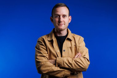 Kahverengi gömlekli mavi arka planda kendine güvenen neşeli bir adamın portresi. Mutluluk duygusu. Hafif gülüşlü bir adam