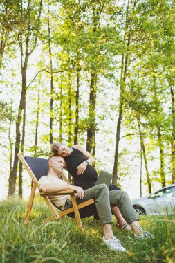 Bir aile çifti, bir erkek ve bir kadın, doğada dinleniyorlar ve bir dizüstü bilgisayarla uzaktan çalışıyorlar. İnternette çalışan sevgili çiftlerin pikniği. Hamile bir kadın kocasıyla birlikte doğada dinleniyor.