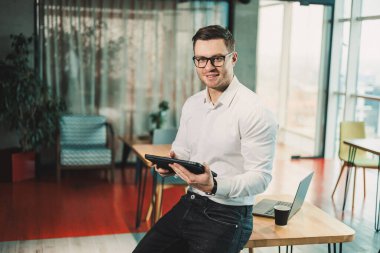 Gözlüklü ve beyaz gömlekli başarılı genç bir adam modern bir çalışma alanında bir proje üzerinde çalışıyor. Erkek işadamı yönetici ofiste çalışıyor..