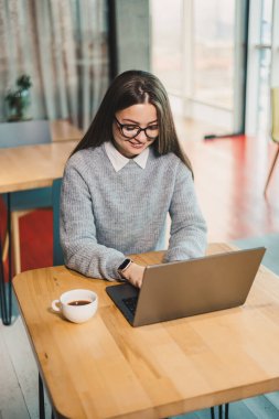 Modern bir iş yerinde masa başında oturmuş dizüstü bilgisayarla çalışan sevimli bir iş kadını. Ofisteki bir kadının çalışma süreci