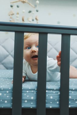 Bebek beşiğin kenarlarından odaya doğru bakmaktadır. Yeni doğmuş küçük bir çocuk çocuklar için bir beşikte yatıyor. Çocukların uyuyabileceği bir yer.