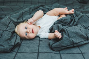 Küçük bir çocuk evde büyük bir yatakta yatıyor. Gri bir yatakta yatan beş aylık bir bebeğin portresi. Neşeli mutlu çocuk.