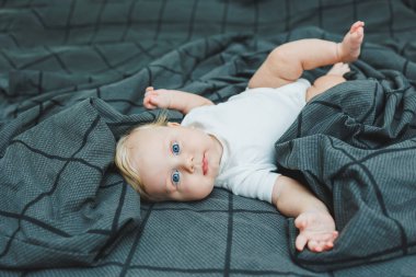 Küçük bir çocuk evde büyük bir yatakta yatıyor. Gri bir yatakta yatan beş aylık bir bebeğin portresi. Neşeli mutlu çocuk.