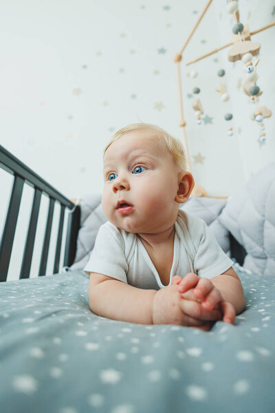 A small child is lying in a crib at home. Portrait of a five-month-old baby lying in a playpen. Cheerful happy child.
