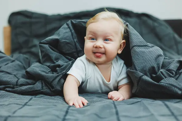A small child is lying on a big bed at home. Portrait of a five-month-old baby lying on a gray bed. Cheerful happy child.
