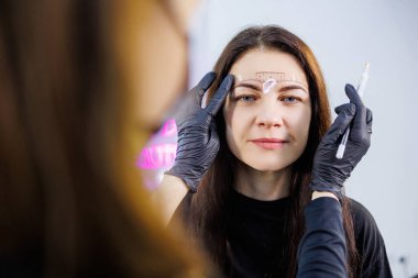 Kalıcı kaş makyajından önce bir kadının yüzünü işaretlemek. Kaş dövmesi. Bir kadının yüzü için güzellik prosedürü