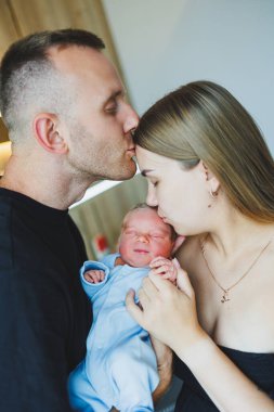 Mutlu genç ebeveynler yeni doğmuş bebeklerini kollarında tutuyorlar. Romper yeni doğmuş bir çocukta. Yeni doğmuş bebek anne ve babanın ellerinde.