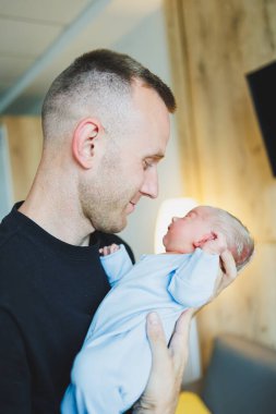 Mutlu genç baba yeni doğmuş bebeğini kollarında tutuyor. Yeni doğmuş bir çocukta Romper.