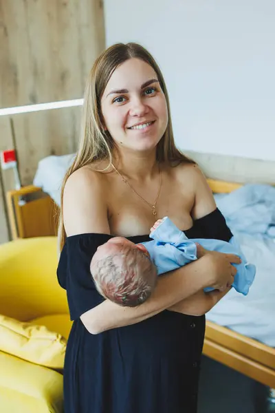 A young happy mother holds her newborn baby in her hands. A mother looks at her little child in her arms