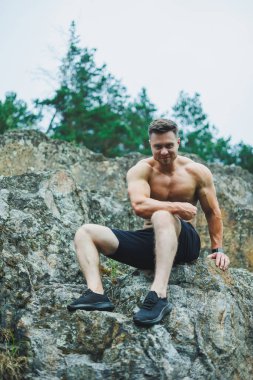 Kayaların arkasındaki genç kaslı adam. Çıplak gövdeli atletik bir adam bir orman kayasının arka planında poz veriyor..