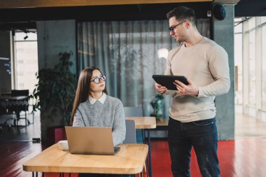 Erkek ve bayan meslektaşlar modern bir ofiste bir proje üzerinde birlikte çalışıyorlar. Ofisteki işçiler uydunun arkasında dizüstü bilgisayarla çalışıyorlar. Astın ve yöneticin.