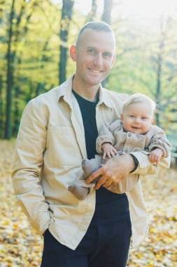 Mutlu genç baba, sıcak bir bahar ya da yaz gününde parkta oğluna sarılıyor. Parkta gün ışığı. Baba oğul doğada aile kavramı.