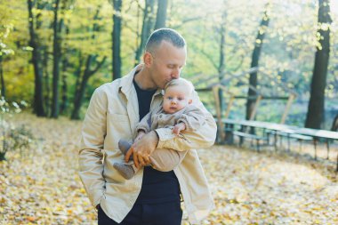 Mutlu genç baba, sıcak bir bahar ya da yaz gününde parkta oğluna sarılıyor. Parkta gün ışığı. Baba oğul doğada aile kavramı.